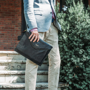 Person holding a black leather briefcase outdoors on stone steps.
