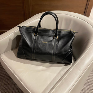 Black leather bag on a white surface with a wooden background