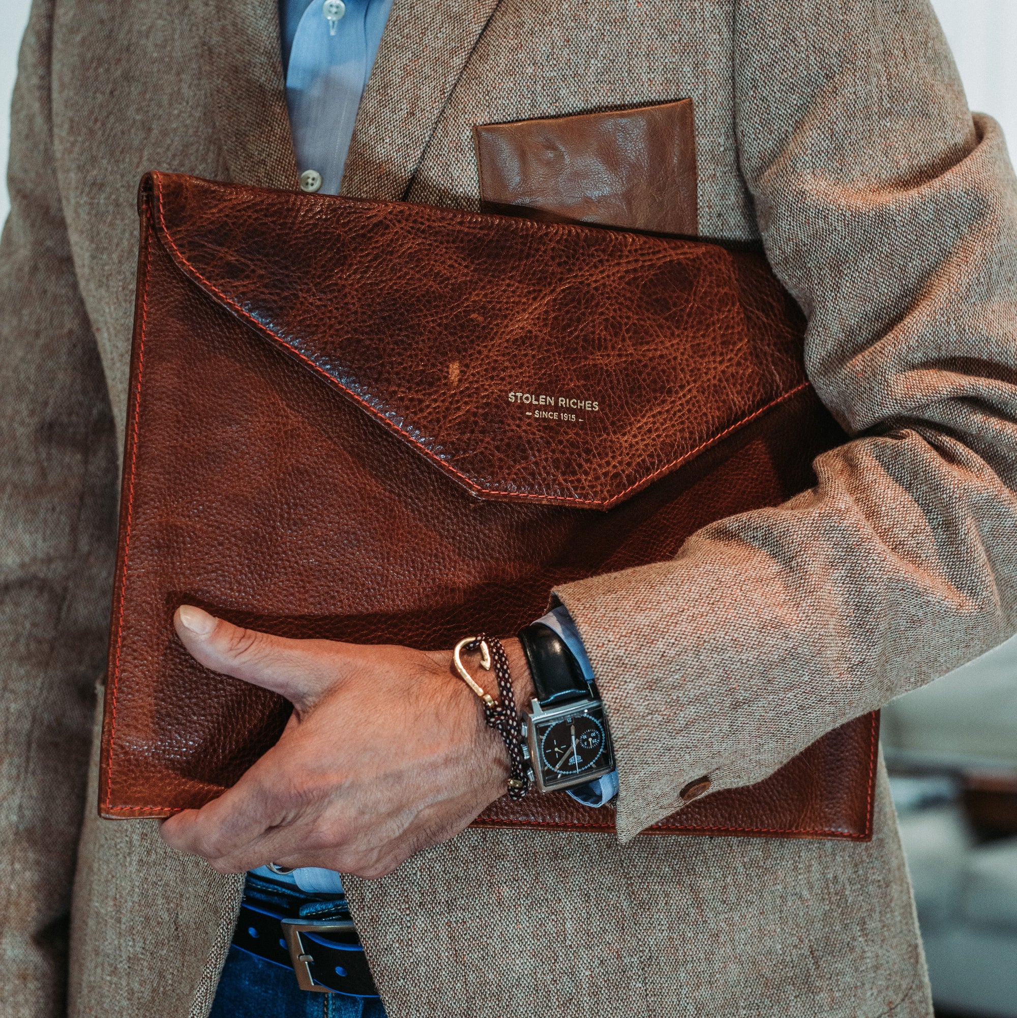 Man holding a brown leather clutch bag with visible brand name.