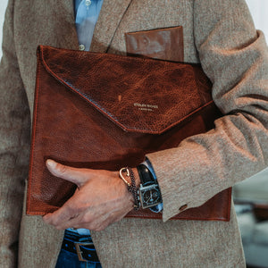 Man holding a brown leather clutch bag with visible brand name.