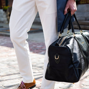 Person holding a black duffel bag on a cobblestone street